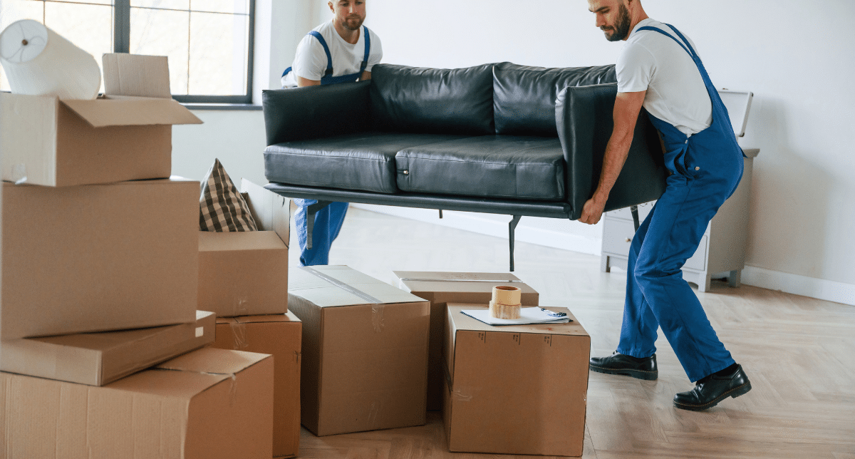 Deux professionnels portent un canapé en cuir noir au milieu de cartons lors d'un débarras de maison