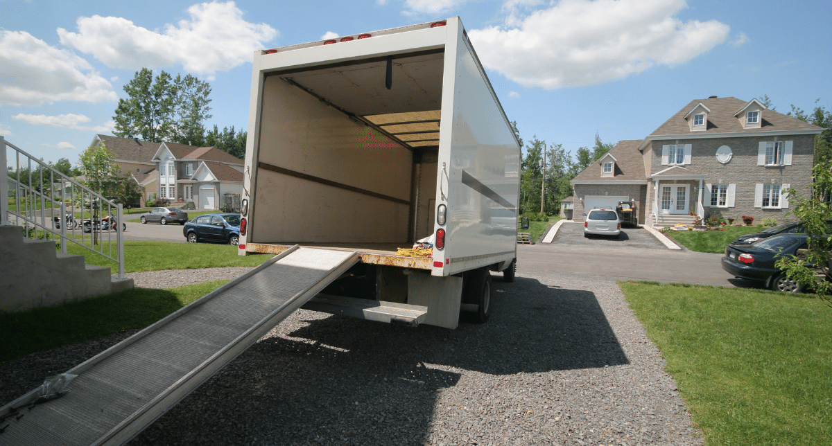 Camion de déménagement blanc ouvert avec sa rampe, garé devant une maison, pour un débarras