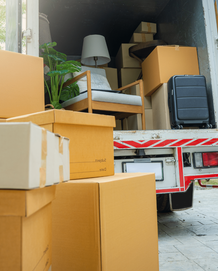 Camion rempli de cartons, d'un fauteuil, d'une lampe et d'une valise, avec des cartons empilés au premier plan